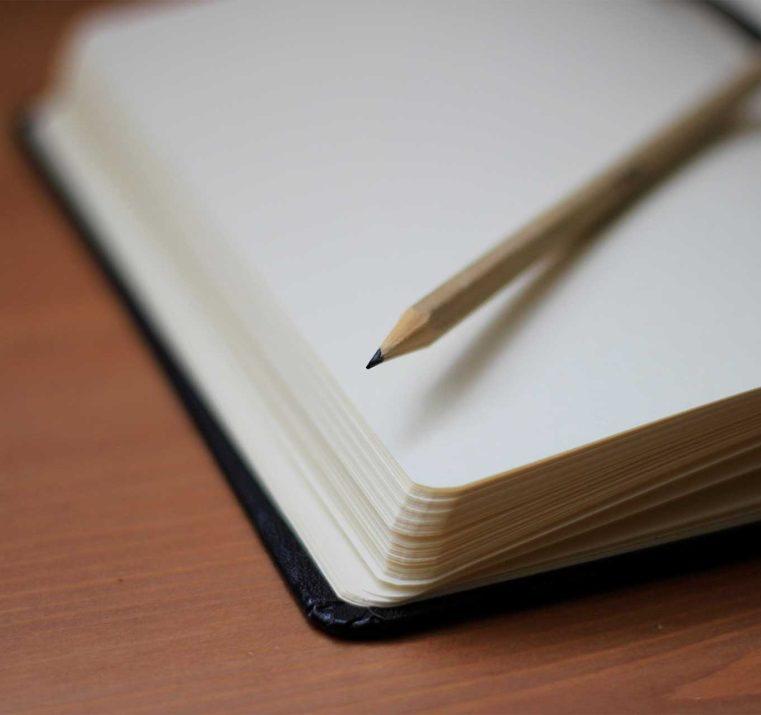 An open book with a pencil placed on its pages, representing writing, note-taking, and the process of reflection or learning.